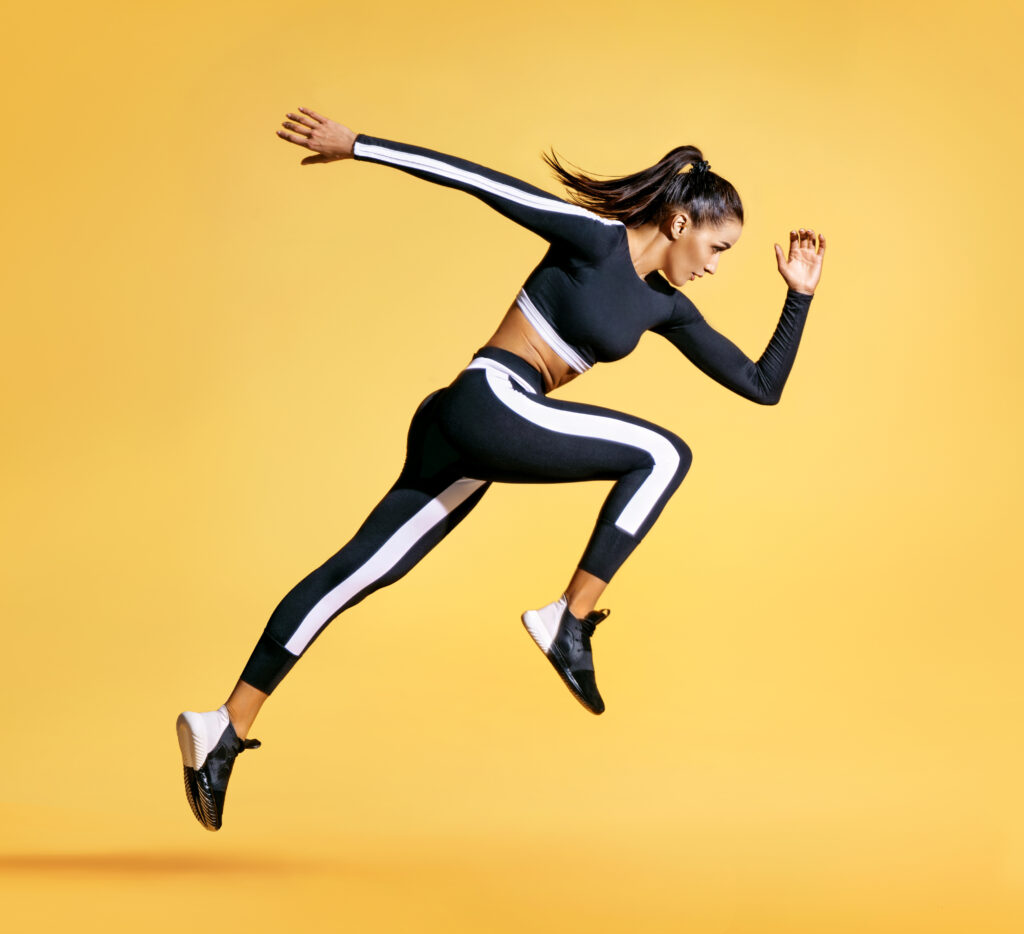 Sporty woman runner in silhouette on yellow background. Photo of attractive woman in fashionable sportswear. Dynamic movement. Side view. Sport and healthy lifestyle